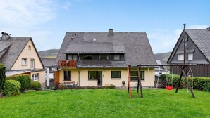 A two-story house with a sloped roof, a balcony, and a front yard with a swing set. - Apartment With Private Terrace in Velmede (Bestwig)