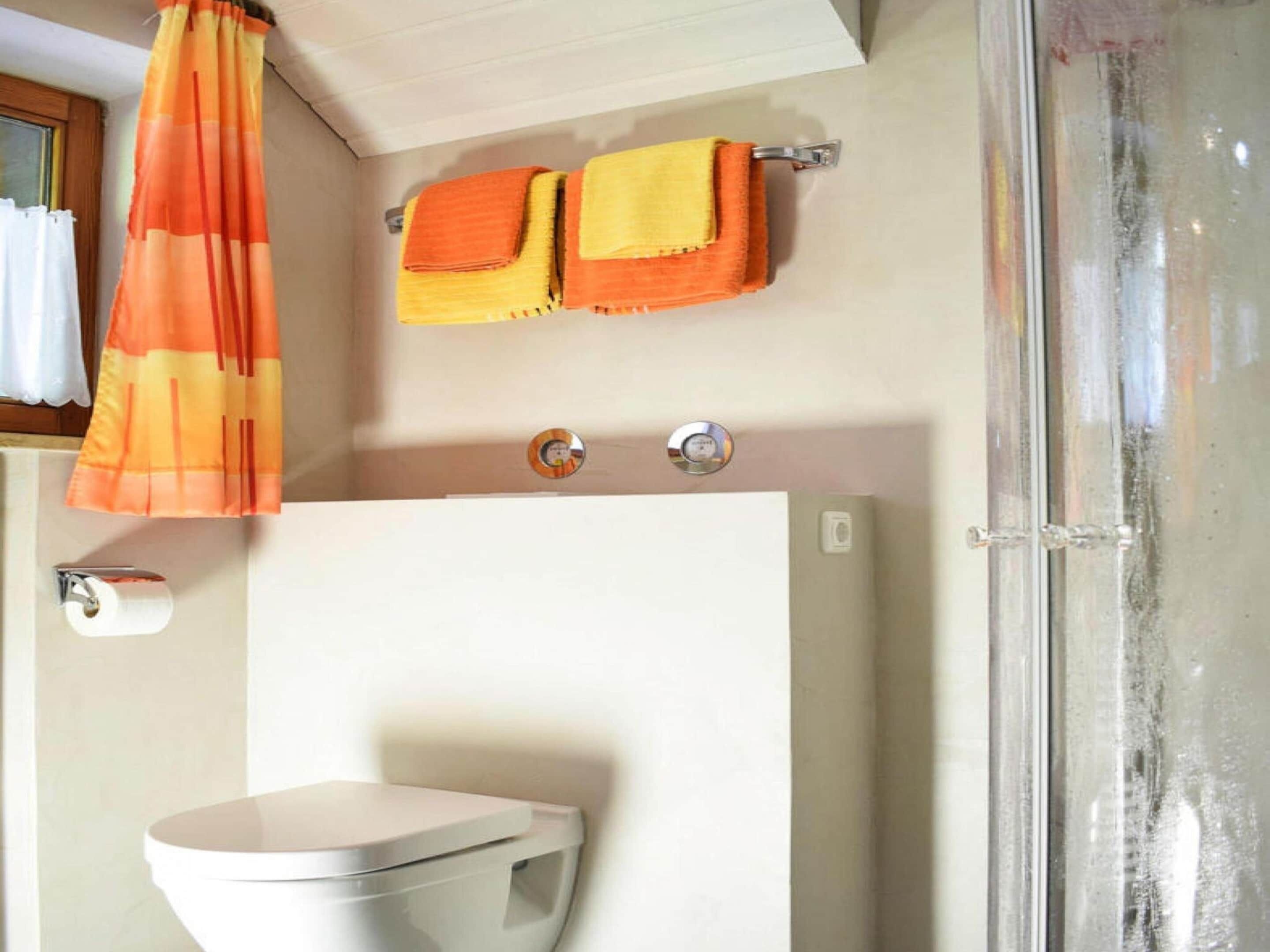 A bathroom with a toilet, a shower curtain, and two towels on a towel rack.