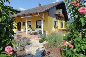 A yellow house with a patio, surrounded by greenery and flowers. - Holiday Home in a spa Town Near Forest (Gleissenberg)