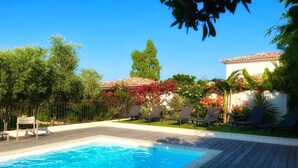 A swimming pool with a wooden deck, surrounded by lush greenery and a white building with a tiled roof. - Villa Maestro Maria 🏡Warm welcome 🧡 heated pool 🌞beach 5' away 🏖️ (Lecci)