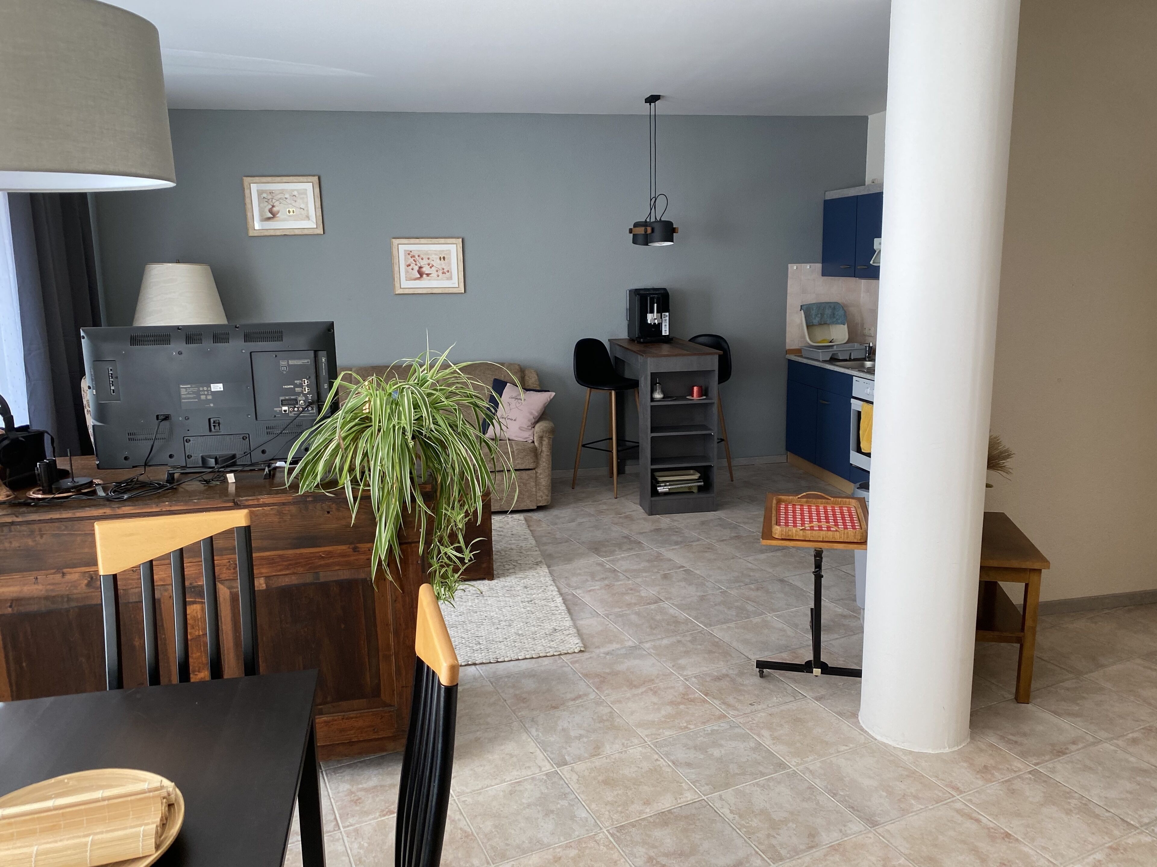 Una sala de estar moderna con un televisor de pantalla plana, una máquina de café, una mesa de comedor y una planta.