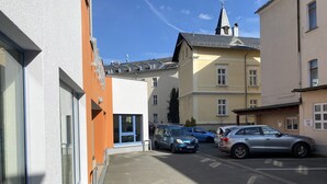Eine schmale Straße mit parkenden Autos, ein Gebäude mit Schild mit Zimmer Nummer 19 und ein Kirchturm im Hintergrund.