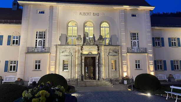 Ein prächtiges Gebäude mit einem Glockenturm, genannt 'Albert Bad', mit einer symmetrischen Fassade, Bogenfenstern und einem zentralen Eingang mit Stufen.
