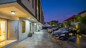 Un edificio moderno con una marquesina, coches aparcados y una entrada bien iluminada.