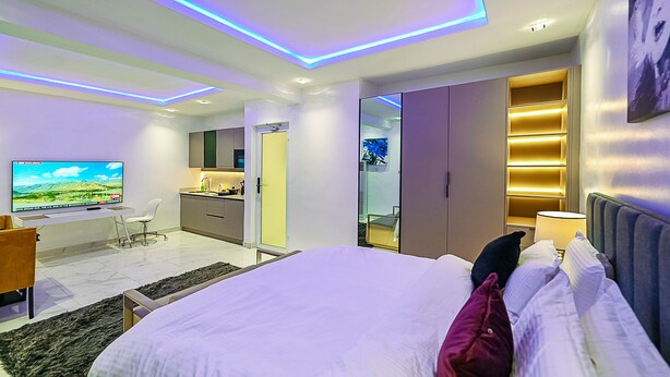 Una habitación de hotel moderna con una cama grande, un escritorio con televisión de pantalla plana, un armario y un baño.