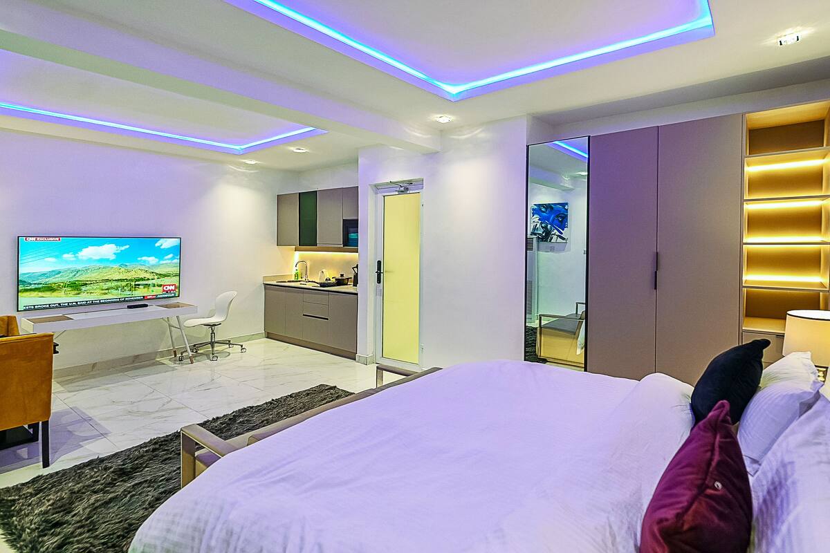 A modern hotel room with a large bed, a desk with a flat-screen TV, a wardrobe, and a bathroom.