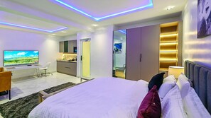 A modern hotel room with a large bed, a desk with a flat-screen TV, a wardrobe, and a bathroom. - The Muse Residences (Lekki)