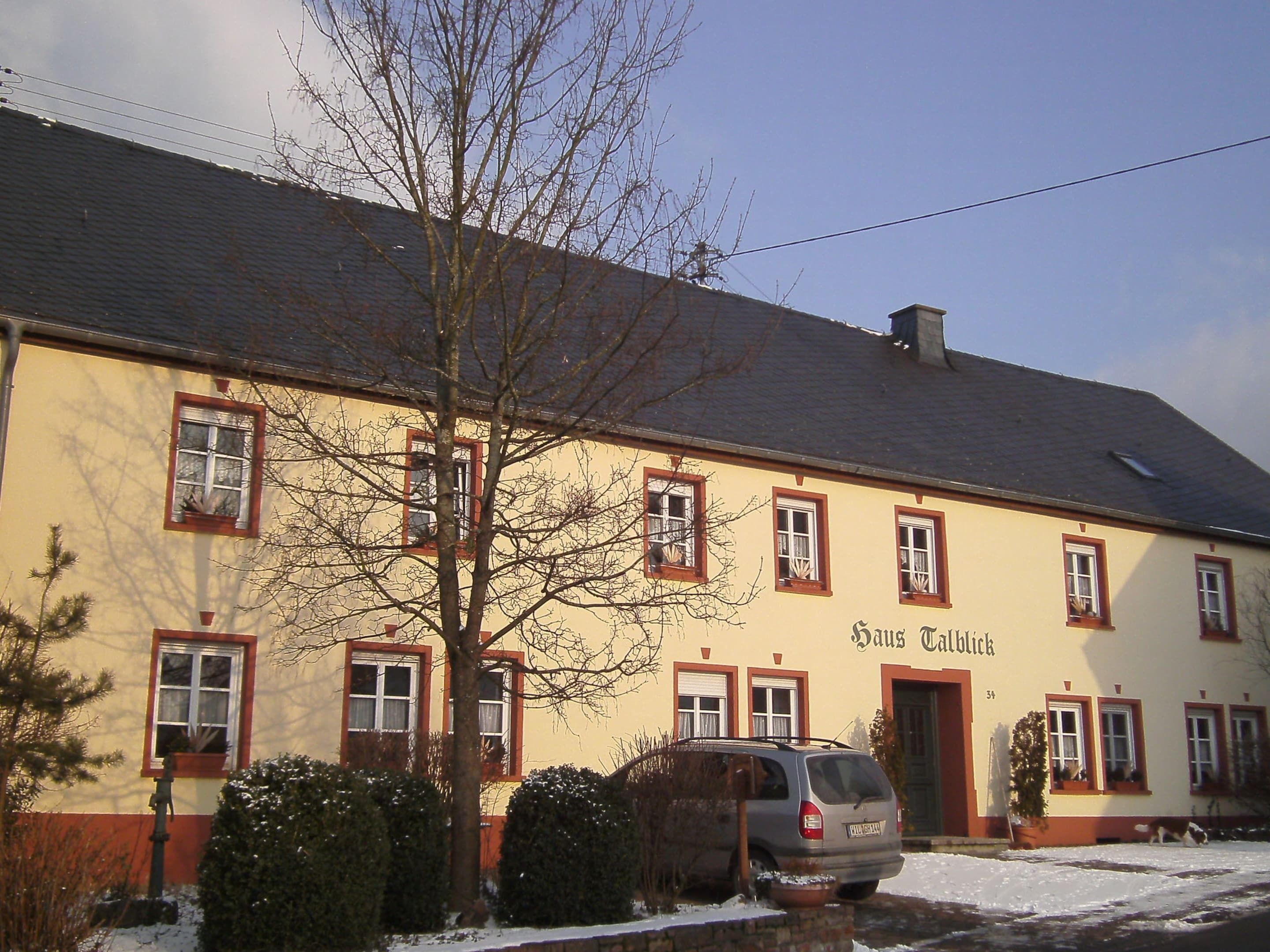 Un bâtiment à deux étages, doté d’une façade jaune et de bordures rouges, portant l’inscription « Haus Tilly ».