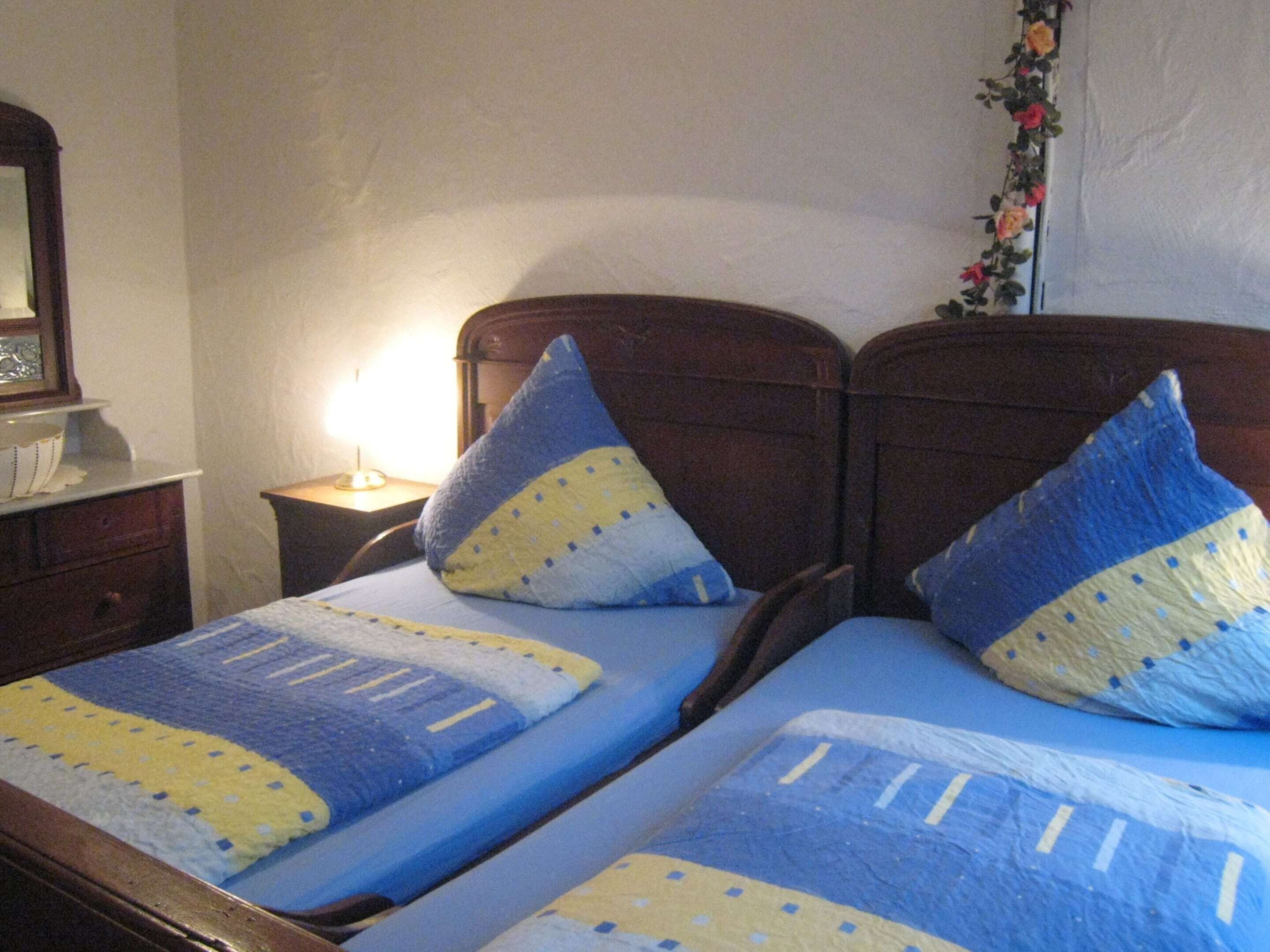A double bed with blue and yellow bedding, a wooden headboard, and a nightstand with a lamp.