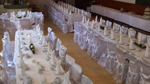 A banquet hall with tables set for a formal event, featuring white tablecloths, folded napkins, and floral centerpieces.