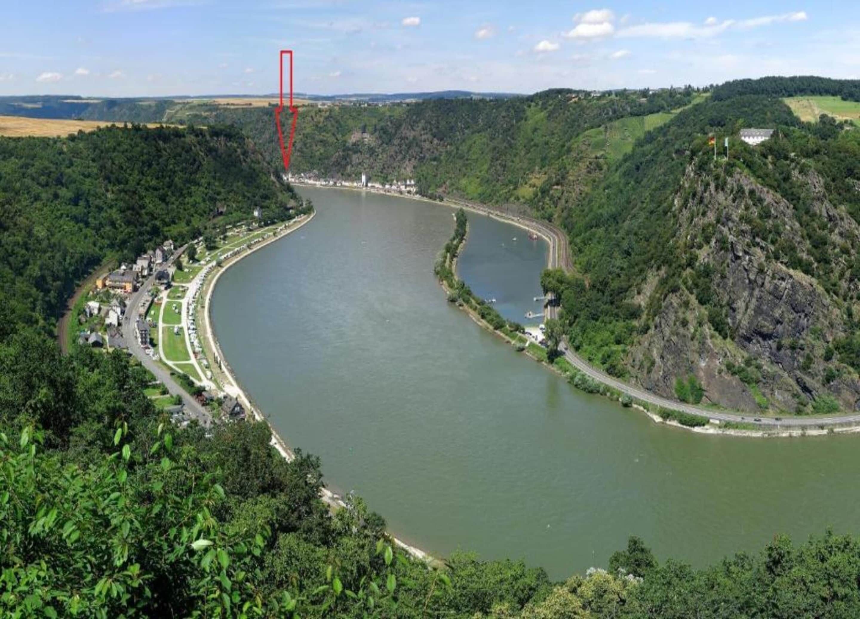 Un fiume serpeggia attraverso una valle, con una città su un lato e una collina boscosa sull'altro.