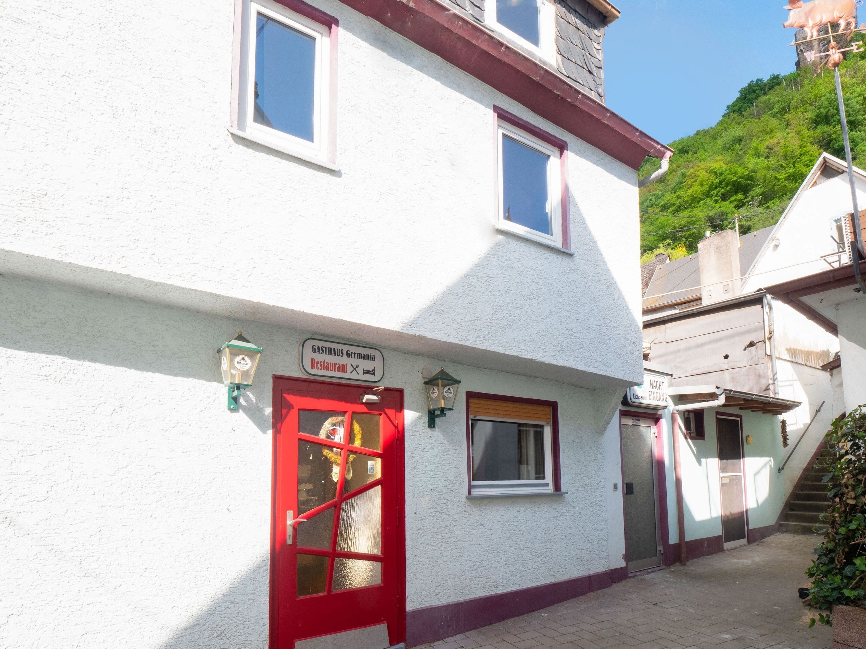 Un edificio con una porta rossa, un cartello che riporta “GASTHAUS Germania Restaurant” e una scala che conduce a un piano superiore.