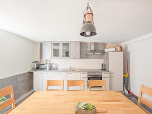 Eine kompakte Küche mit weißen Schränken, einer Mikrowelle, einem Herd und einem Spülbecken. Vier Holzstühle stehen um einen Tisch mit einer Pflanze als Mittelstück.