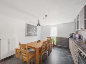 A modern kitchen with a dining area, featuring a wooden table and chairs, a potted plant, and a view of the city through a window. - Ferienwohnung Am Marktplatz in Herbolzheim (Herbolzheim)