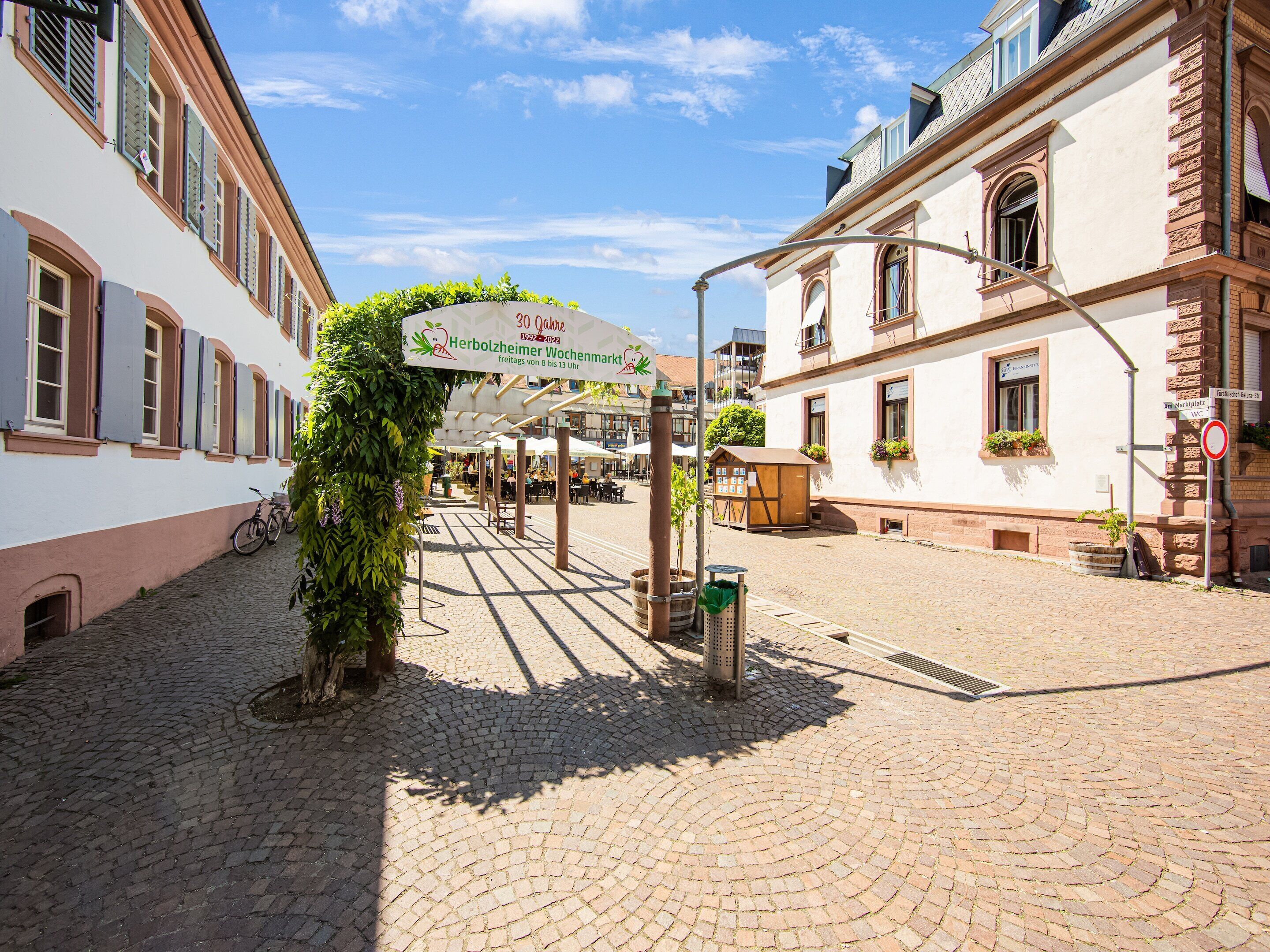 A cobblestone street with a sign for a local market, buildings with traditional architecture, and a bicycle parked on the side.