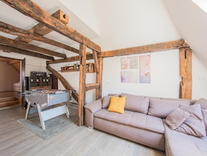 Ein Loft-Zimmer mit freiliegenden Holzbalken, einem Kicker, einer Couch mit Kissen und einer Treppe, die zu einer weiteren Ebene führt.