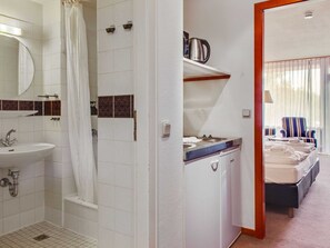 A hotel bathroom with a sink, shower, and a view of a bedroom with a bed and a chair. - Ferienwohnung in Hahnenklee (Goslar)