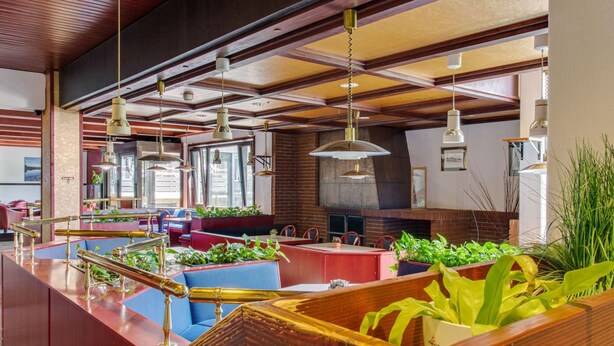 Un restaurante espacioso con techos altos, vigas de madera y múltiples lámparas colgantes.