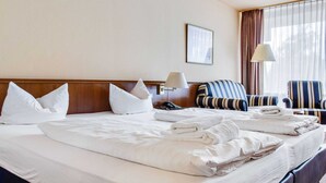 Una habitación de hotel con una cama grande, dos mesitas de noche, un escritorio con lámpara, una silla y una ventana con cortinas.