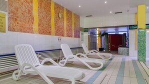 Zona de piscina con sillas de descanso, suelo de baldosas y una pared con reloj y señalización.