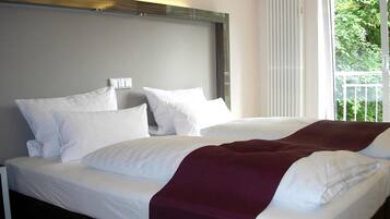 Ein Hotelzimmer mit einem großen Bett, weißer Bettwäsche und Blick auf Grün durch das Fenster.