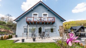 A two-story house with a balcony, a patio with outdoor furniture, and a garden. - Luxurious Holiday Home With a Nice Private Garden (Anschau)