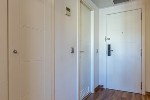 Un couloir avec une porte blanche, un interphone et une grille d’aération sur le mur.