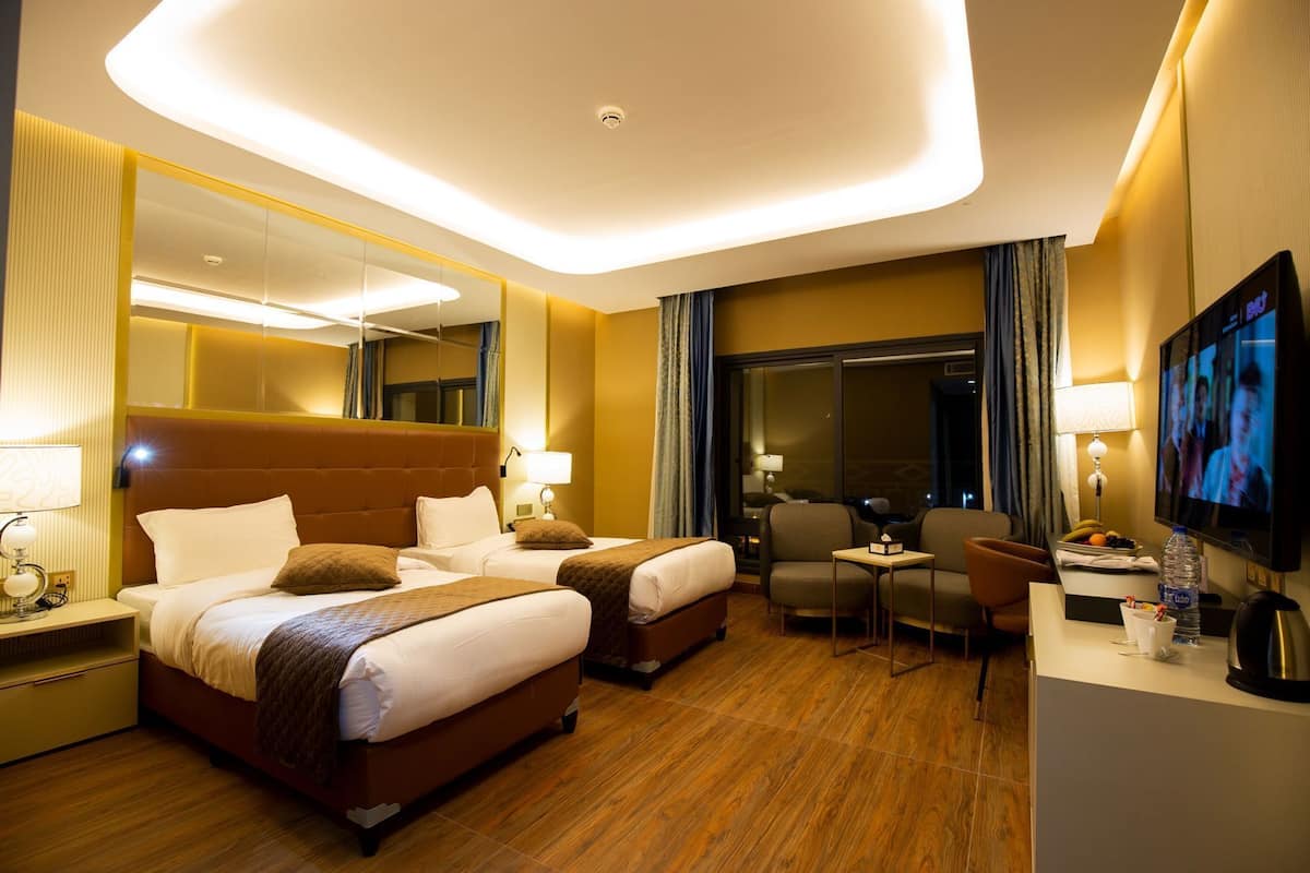 Habitación de hotel con dos camas, un escritorio, un televisor y un ventanal amplio.
