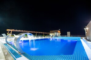 A nighttime swimming pool with a circular water feature, lounge chairs, and a covered seating area. - Petra Moon Luxury Hotel (Wadi Musa)
