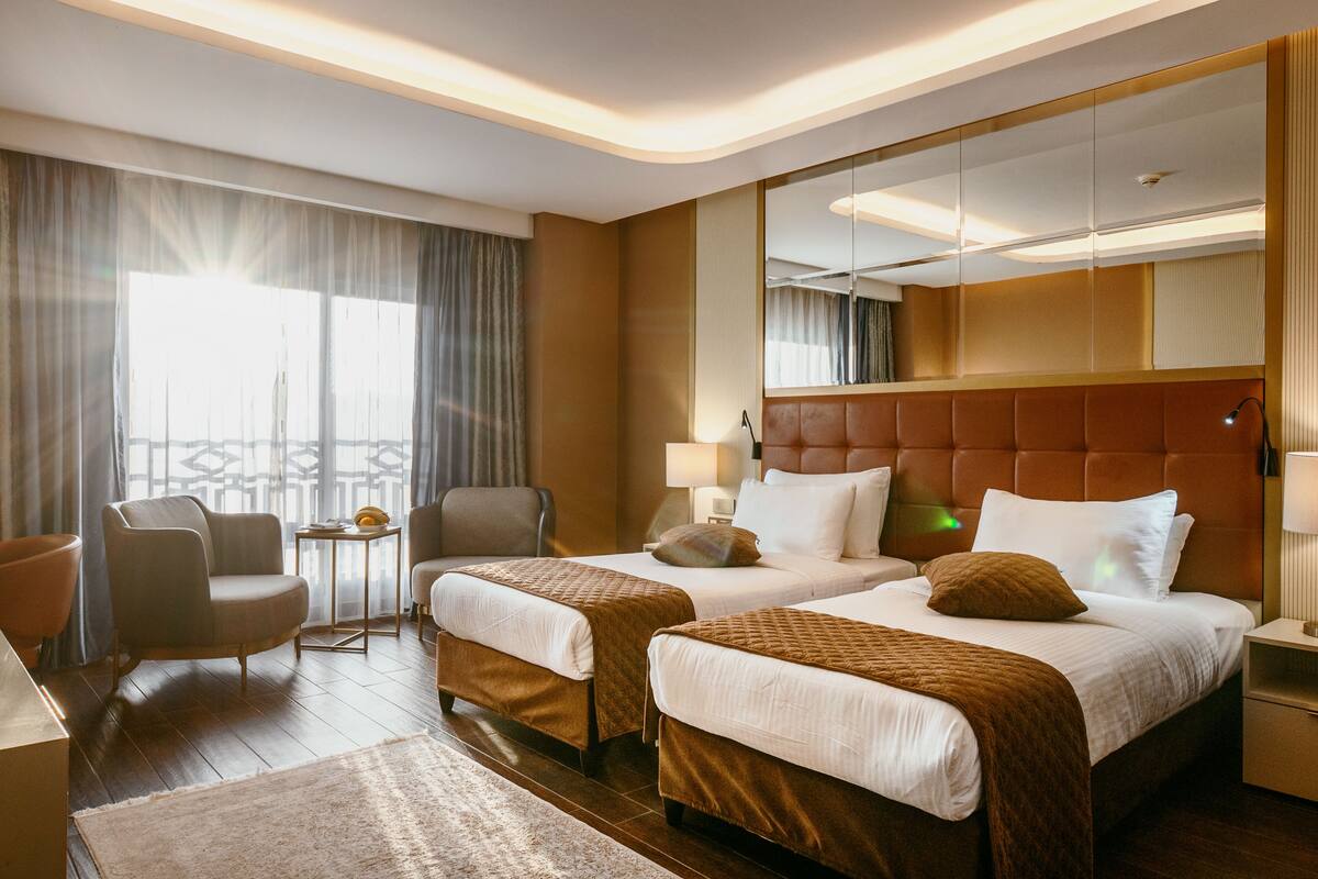 Habitación de hotel con dos camas, zona de estar con una silla, una mesita y un espejo grande.