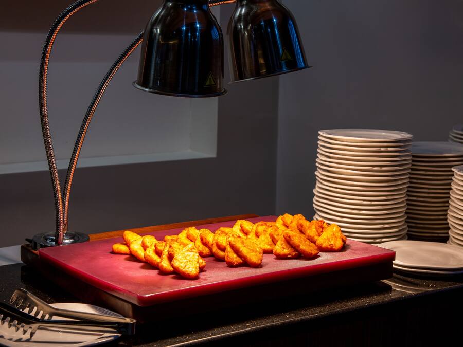 Une table de buffet avec un plateau de service rouge sur lequel sont disposés des amuse-gueules dorés et bruns, entourée d’assiettes blanches empilées et d’une pile de bols.