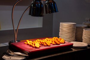 A buffet table with a red serving tray holding golden-brown appetizers, surrounded by stacked white plates and a stack of bowls.