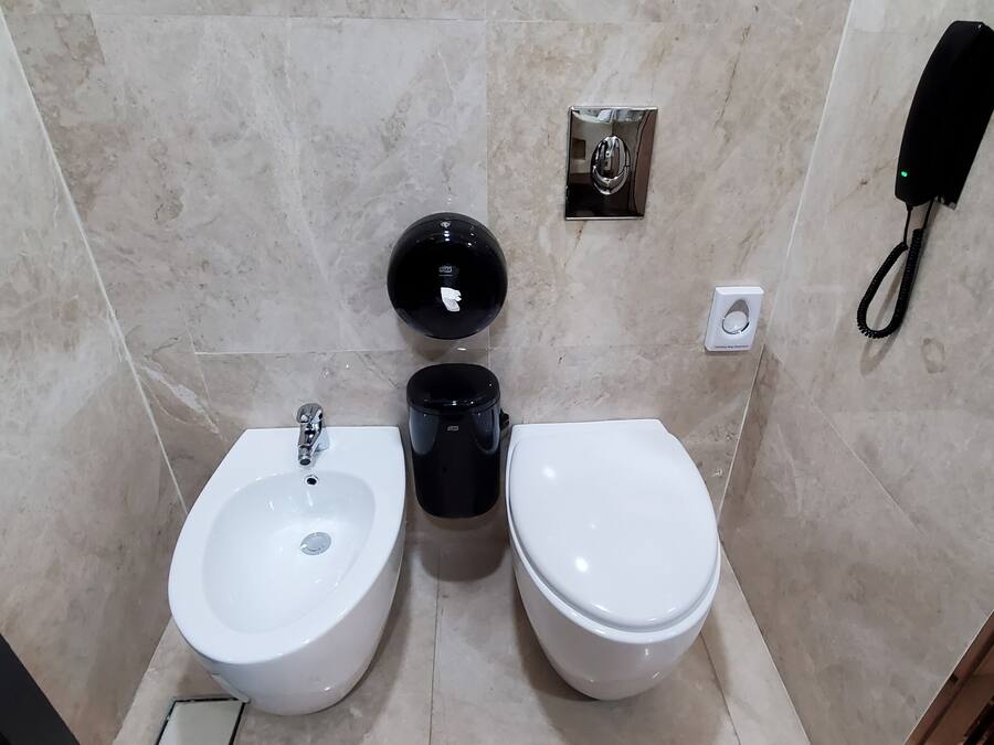 Un baño moderno con un bidé, inodoro y dispensador de gel hidroalcohólico.