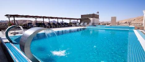 Piscina con cascada, sillones de descanso y vistas a montañas.