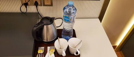 A kitchen counter with a kettle, a water bottle, two white mugs, and packets of coffee creamer.