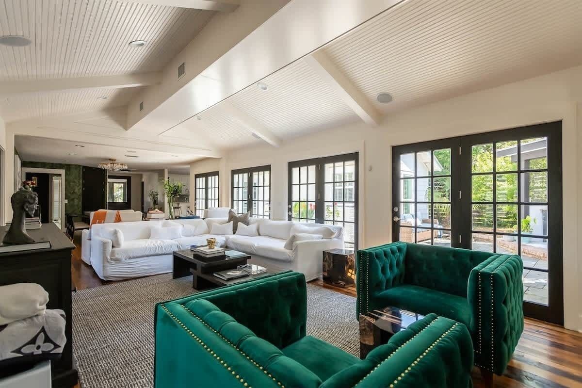 A spacious living room with a white sofa, green armchairs, and a large window with a view of greenery.