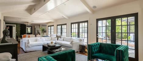 A spacious living room with a white sofa, green armchairs, and a large window with a view of greenery.