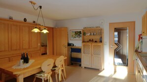 A kitchen with wooden cabinets, a dining table with chairs, and a refrigerator. - Ferienwohnung im Bayerischen Wald mit Sauna (Drachselsried)