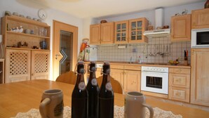 A kitchen with wooden cabinets, a stove, and a dining table with mugs and bottles. - Ferienwohnung im Bayerischen Wald mit Sauna (Drachselsried)