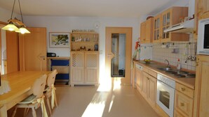 A kitchen with wooden cabinets, a dining table with chairs, and a hanging light fixture. - Ferienwohnung im Bayerischen Wald mit Sauna (Drachselsried)
