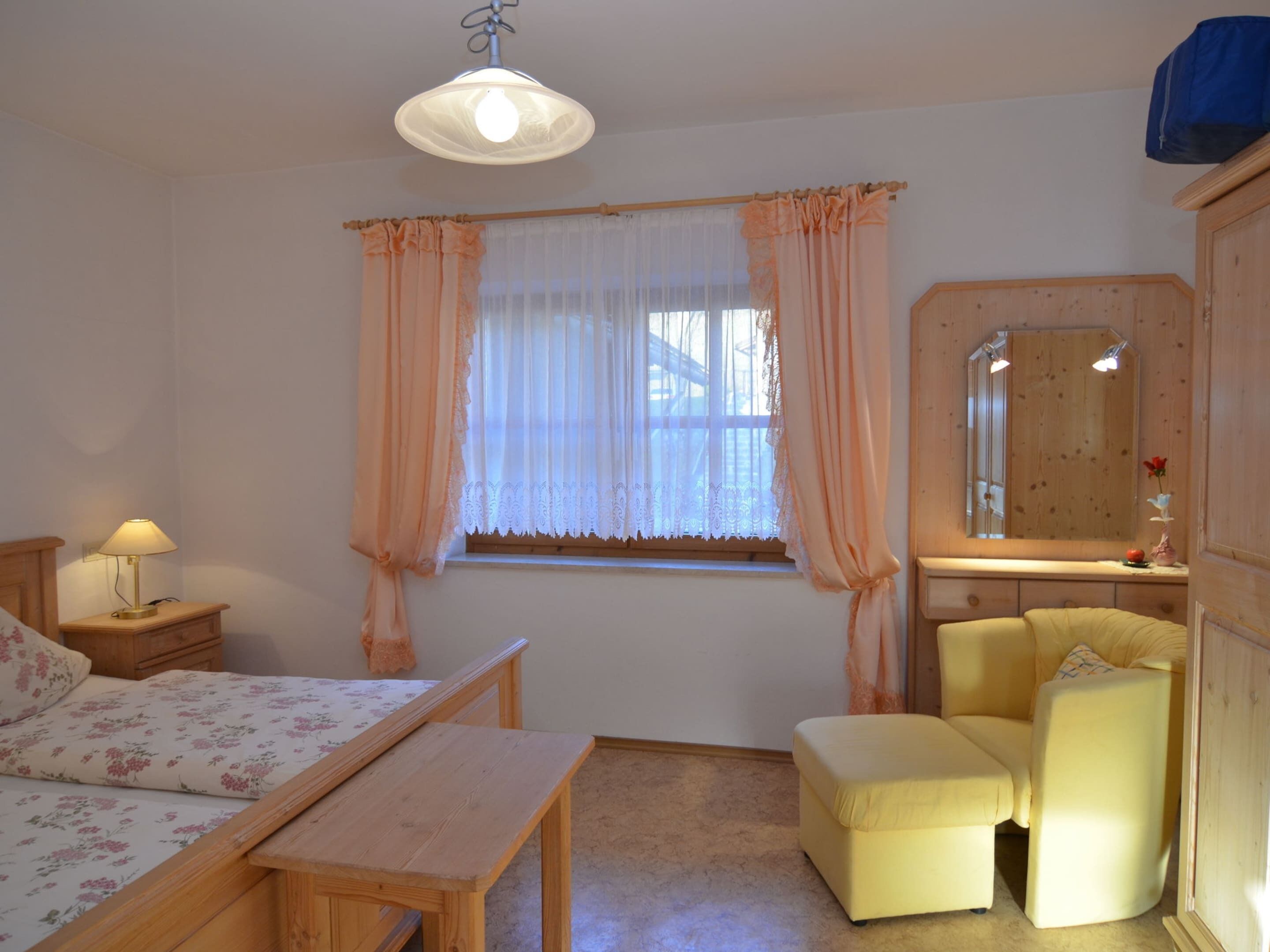 A bedroom with a bed, bedside table, lamp, chair, and a window with curtains.