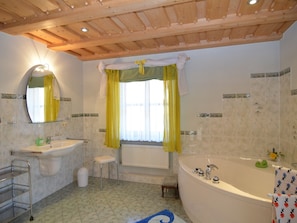 A bathroom with a bathtub, a sink, a mirror, and a window with yellow curtains.