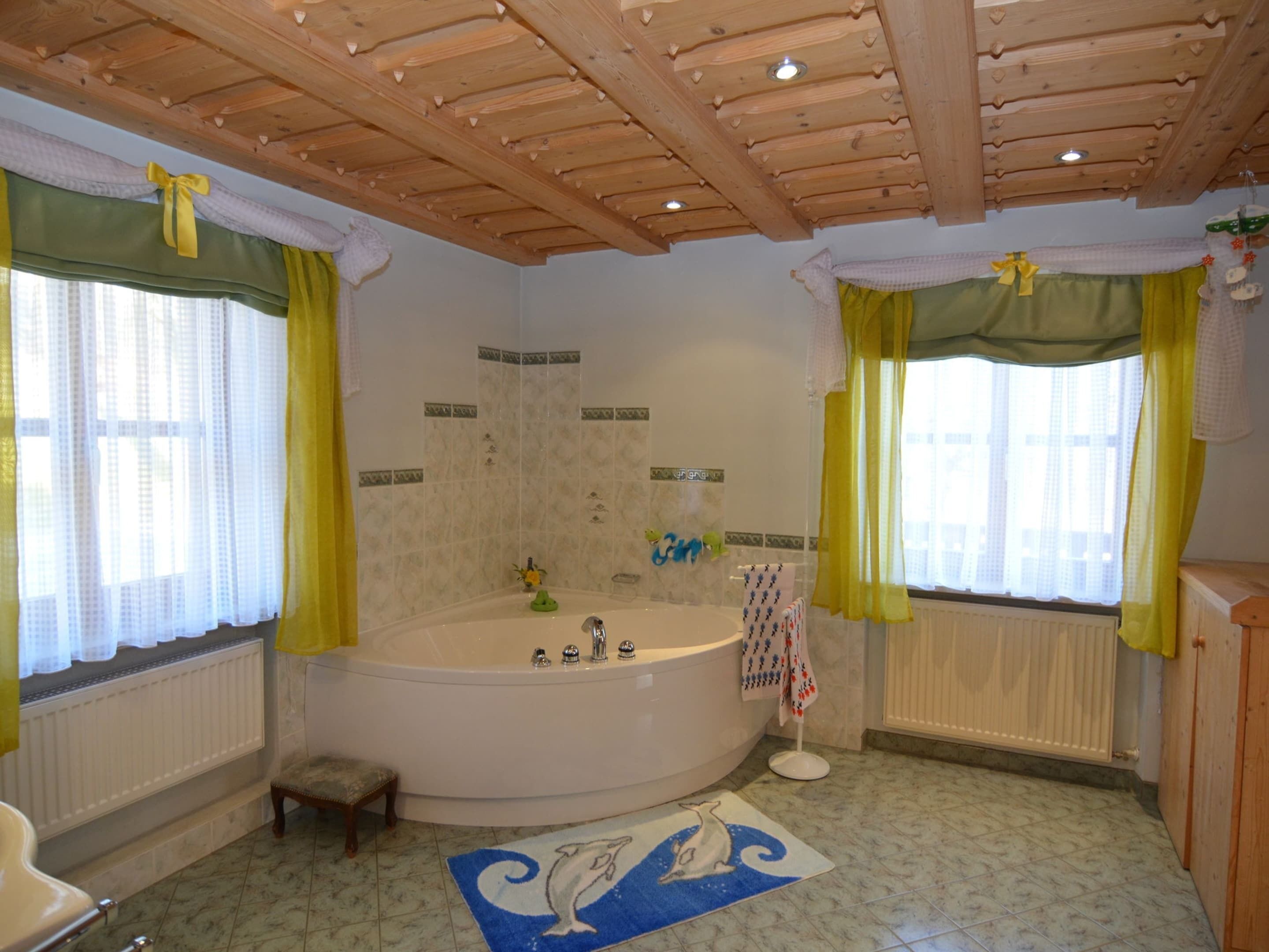 Een badkamer met een groot bad, houten balken in het plafond en een vloerkleed met dolfijnen.