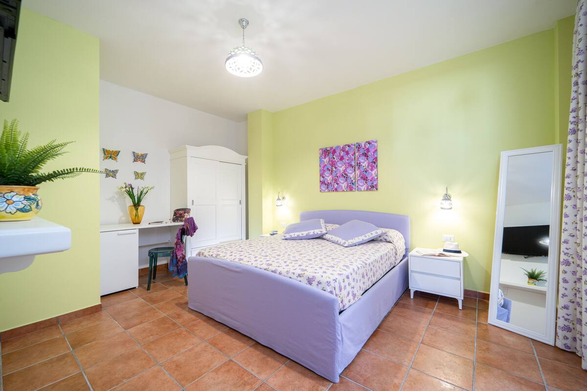 A bedroom with a bed, bedside tables, a desk, and a mirror.