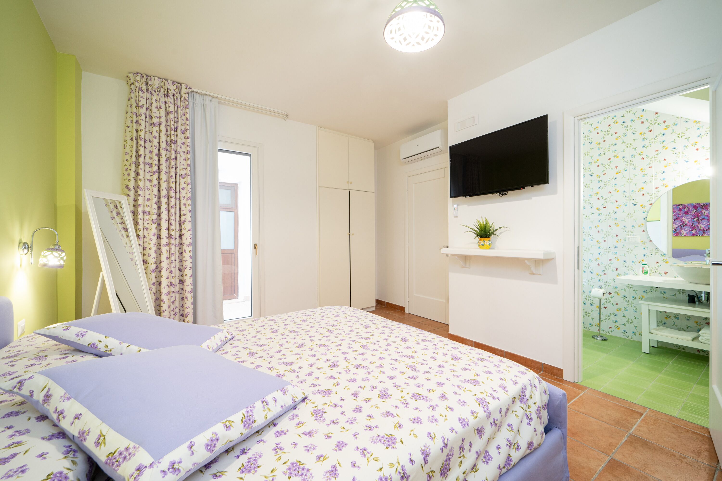 A bedroom with a bed, a TV, a bathroom with a mirror, and a green wall.