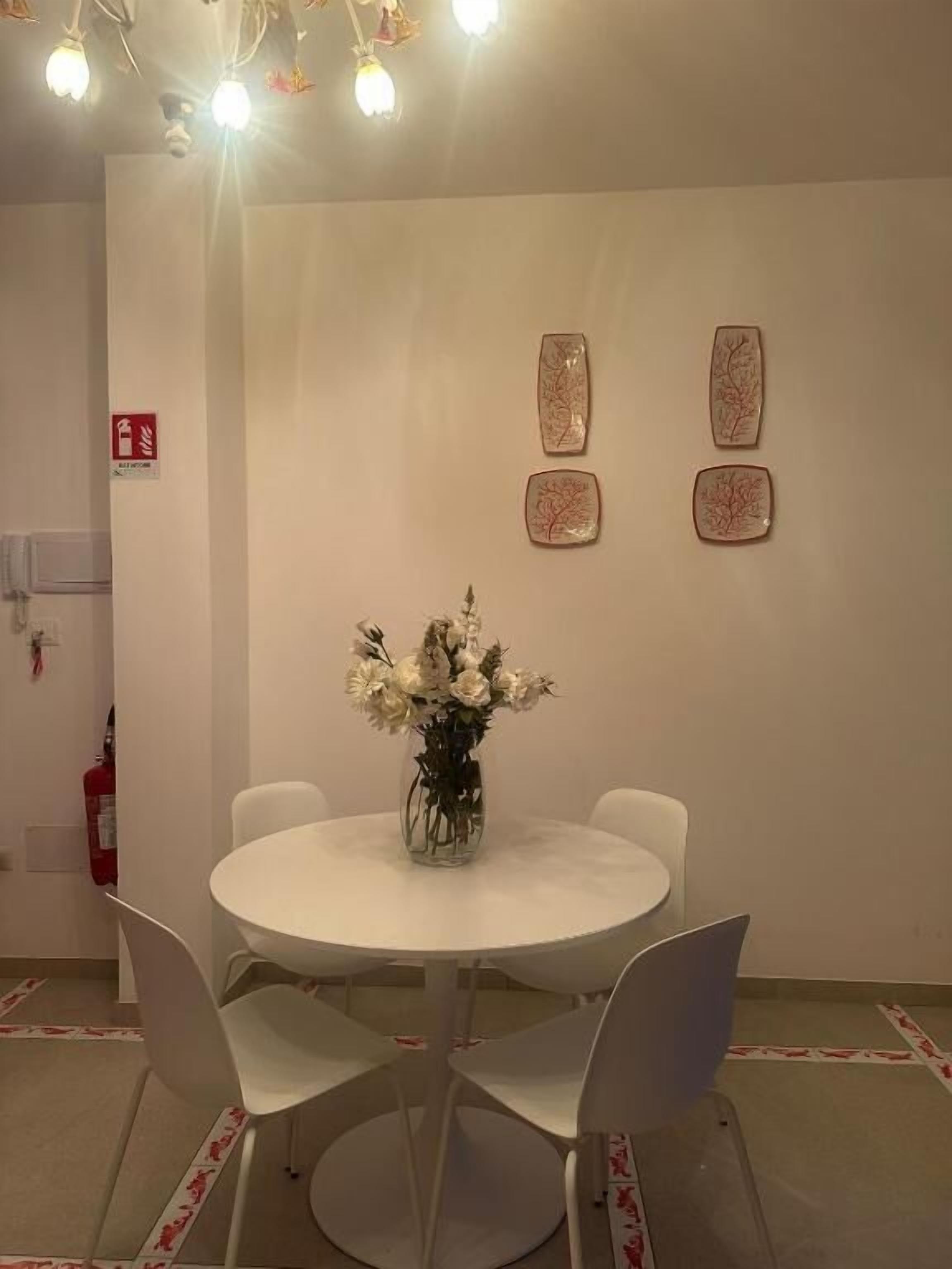 A conference room with a round table, white chairs, and a vase of flowers. There are two wall-mounted artworks and a fire extinguisher on the wall.