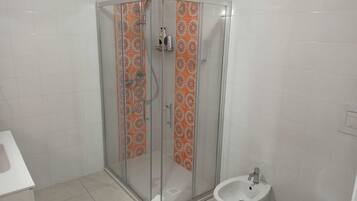 A bathroom with a glass-enclosed shower, a bidet, and a white sink.