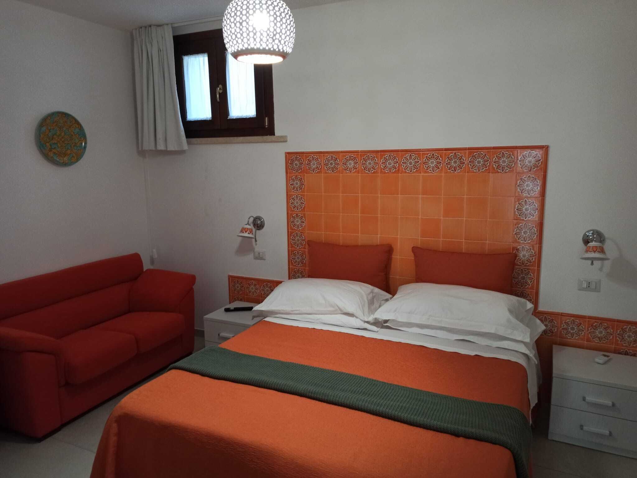 Ein Schlafzimmer mit einem Bett, einem roten Sofa, einem Nachttisch, einer Lampe und einem Wanddekor.