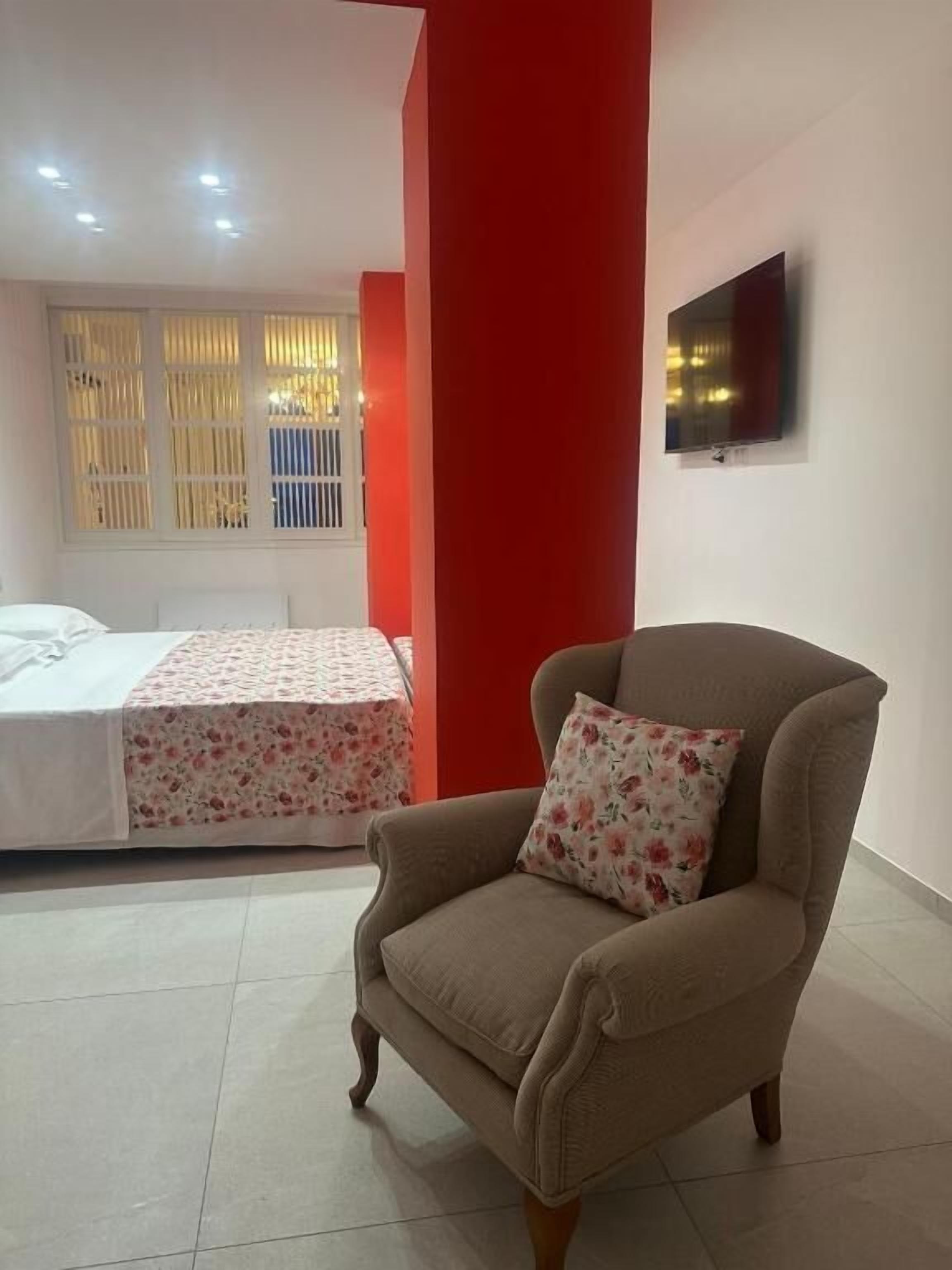 A bedroom with a bed, a chair, and a TV on the wall.