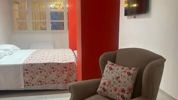 A bedroom with a bed, a chair, and a TV on the wall.